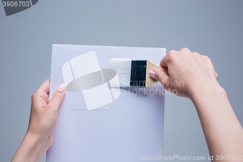 Image of Hands holding painting brush on white canvas