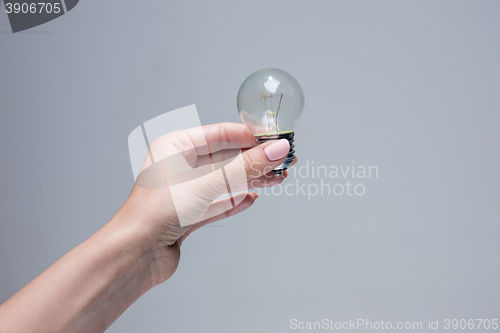 Image of Hand holding an incandescent light bulb on gray background