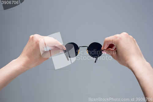Image of The female hands holding sunglasses on gray background.