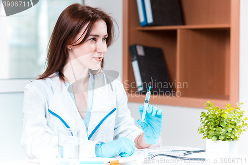 Image of The hand in blue glove holding syringe against white medical gown 