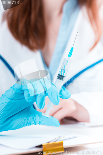 Image of The hand in blue glove holding syringe against white medical gown 