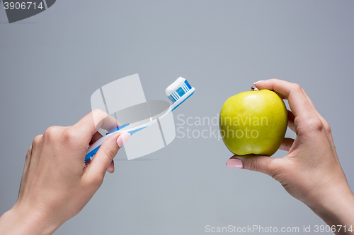 Image of Toothbrush and apple in woman\'s hands on gray