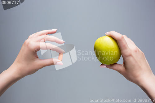 Image of The female hands with apple and pills 