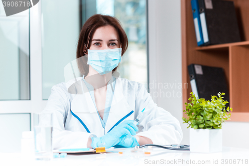 Image of The hand in blue glove holding syringe against white medical gown 