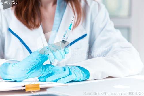 Image of The hand in blue glove holding syringe against white medical gown 