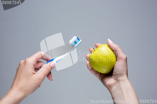 Image of Toothbrush and apple in woman\'s hands on gray