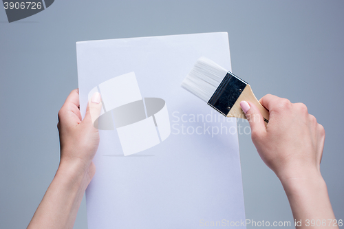 Image of Hands holding painting brush on white canvas