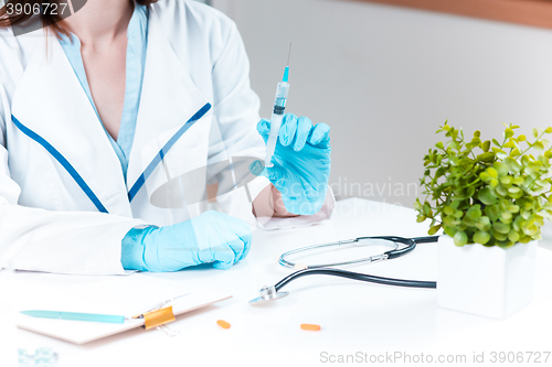 Image of The hand in blue glove holding syringe against white medical gown 