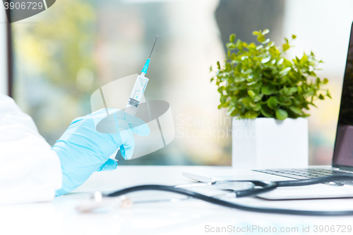 Image of The hand in blue glove holding syringe against white medical gown 