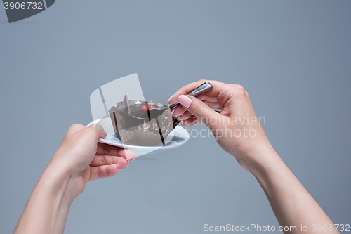 Image of Female hands keeping cake with spoon on gray