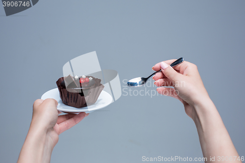 Image of Female hands keeping cake with spoon on gray