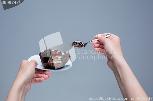 Image of Female hands keeping cake with spoon on gray