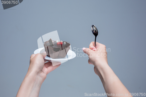 Image of Female hands keeping cake with spoon on gray
