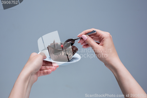 Image of Female hands keeping cake with spoon on gray