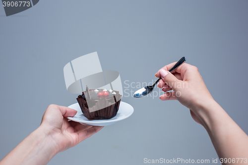 Image of Female hands keeping cake with spoon on gray