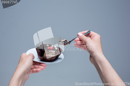 Image of Female hands keeping cake with spoon on gray