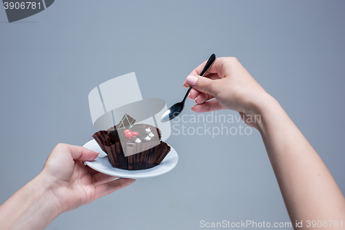 Image of Female hands keeping cake with spoon on gray