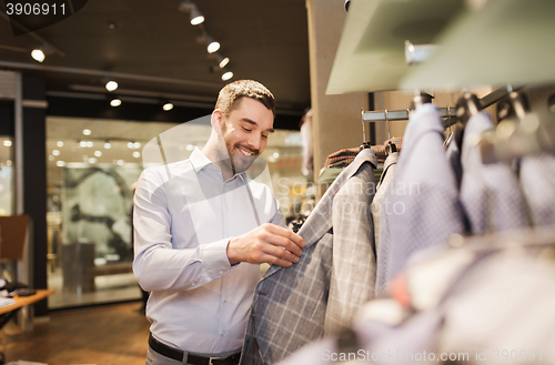 Image of happy young man choosing clothes in clothing store