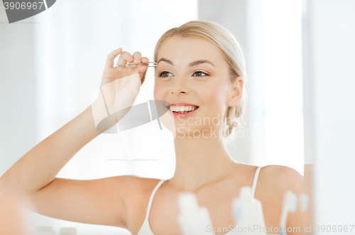 Image of woman with tweezers tweezing eyebrow at bathroom