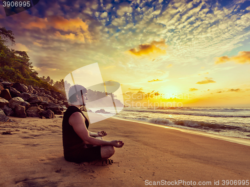 Image of Young sporty fit man doing yoga meditating on tropical beach