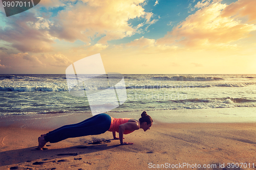 Image of Woman practices yoga asana Chaturanga Dandasana at the beach