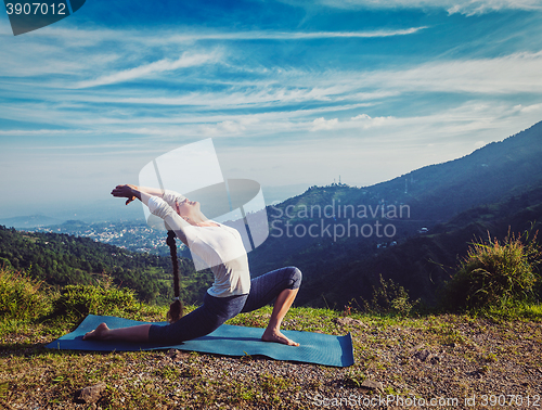 Image of Sporty fit woman practices yoga Anjaneyasana in mountains