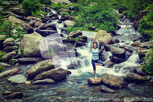 Image of Woman in  yoga asana Vrikshasana tree pose at waterfall outdoors