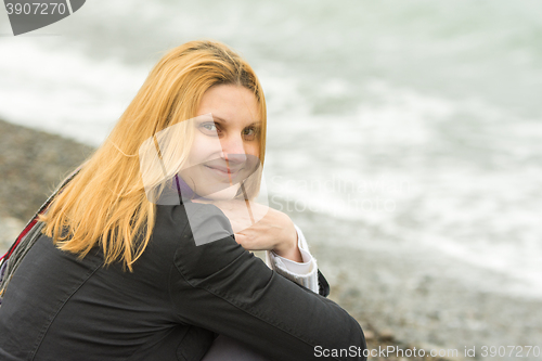 Image of Portrait of sitting on the beach smiling young woman in cold weather