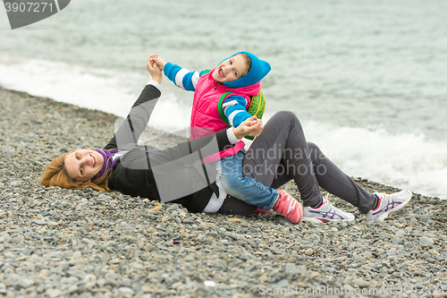 Image of Five-year girl with her mother having fun on the beach pebble beach in cold weather