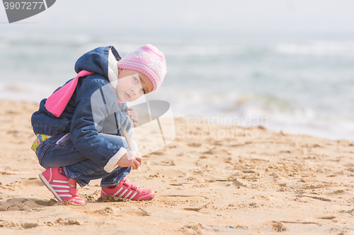 Image of Five-year girl in the spring of the pen draws on the sand by the sea, and looked into the frame