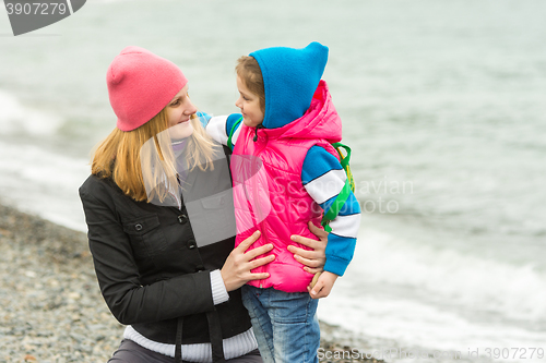 Image of  Mother hugging little daughter and tenderly looking at her on the beach in cold weather