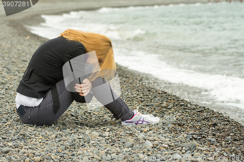 Image of Girl in a cool day on the beach sits thoughtfully with his face buried in his knees