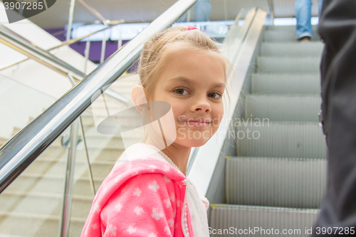 Image of Seven-year girl lying down on an escalator in a mall with a smile look in the frame