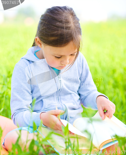 Image of Little girl is reading a book outdoors