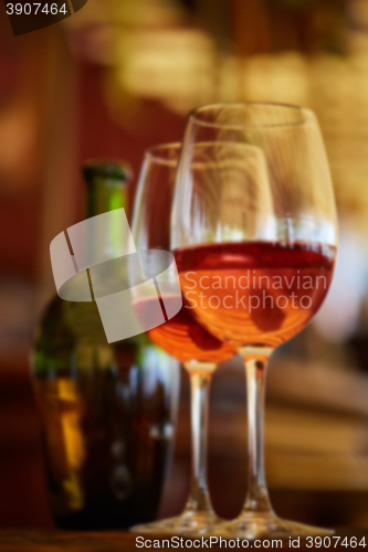 Image of two glasses filled with red wine and bottle in background