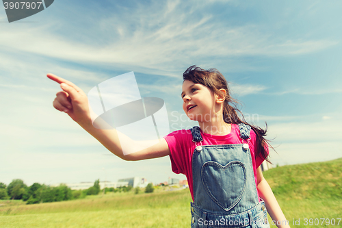 Image of happy little girl pointing finger on summer field