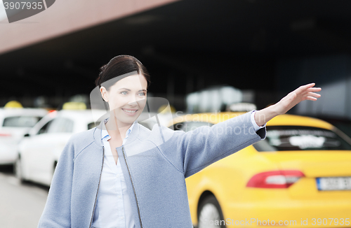 Image of smiling young woman waving hand and catching taxi