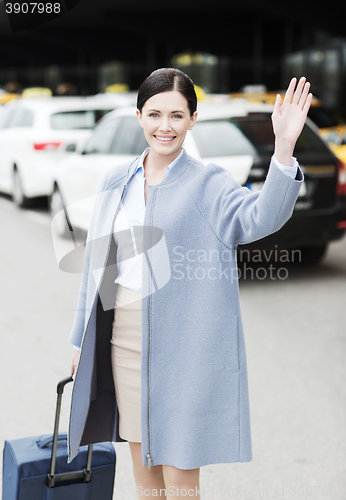 Image of smiling young woman with travel bag waving hand