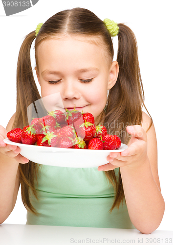 Image of Cheerful little girl is smelling strawberries
