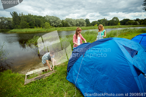 Image of group of smiling friends setting up tent outdoors