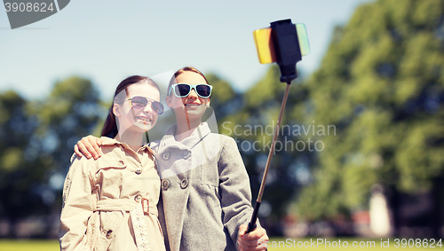 Image of happy girls with smartphone selfie stick in park