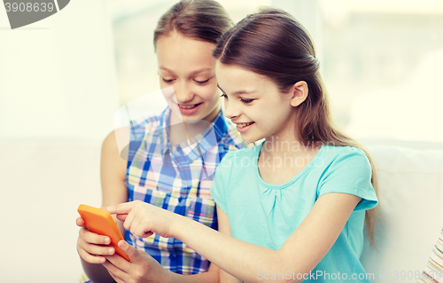 Image of happy girls with smartphones sitting on sofa