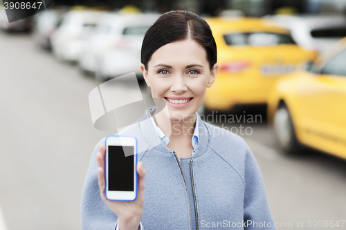 Image of smiling woman showing smartphone over taxi in city