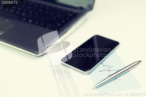 Image of close up of smartphone, laptop and pen on table