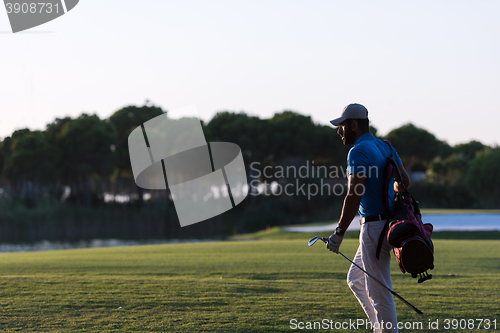 Image of golfer  walking and carrying golf  bag at beautiful sunset