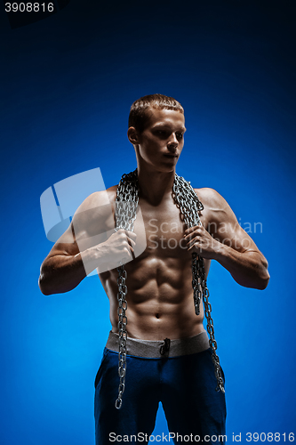 Image of Muscular guy with chains on his shoulders against a blue wall