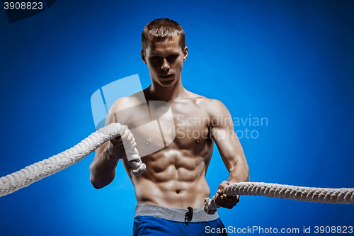 Image of Fit young man with beautiful torso and a rope on blue background