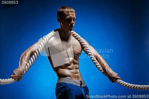 Image of Fit young man with beautiful torso and a rope on blue background