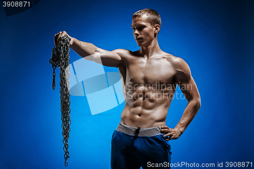 Image of Muscular guy with chains on his shoulders against a blue wall