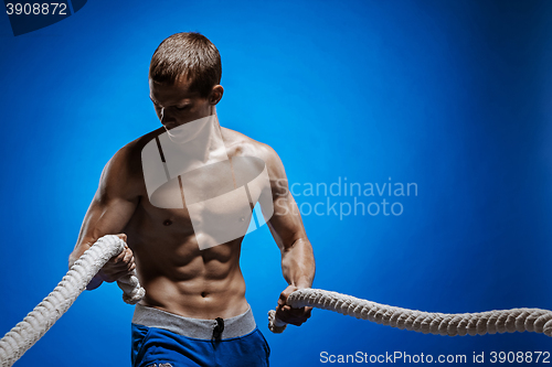 Image of Fit young man with beautiful torso and a rope on blue background